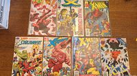 Seven assorted X-Men comic books laid out on a wood table, showing colorful front covers with multiple characters and titles.