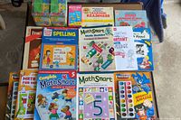 Top-down photo showing 13 assorted colorful kids workbooks arranged in rows, titles visible including MathSmart, Spelling, Learning Readiness, and handwriting book with Bob the Builder.