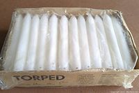 Top view of a large cardboard box containing around 50 white torpedo-shaped candles tightly packed in clear plastic wrapping, unopened and in good condition.