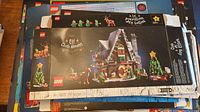 Photo shows stacked LEGO empty boxes including the Elf Club House Christmas set with image of house, Christmas tree, elf figures, and reindeer, in intact condition.