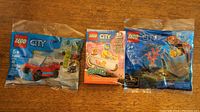 Three sealed LEGO City sets displayed on wood surface showing front packaging