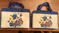 Two new rectangular pansy bags side by side on a wooden surface showing floral pansy and butterfly design on cream background with navy blue sides and handles.