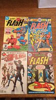 Top view of all four The Flash comics arranged in two rows on a wooden table showing varied cover art and era styles.