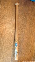 Photo of the entire mini wooden bat showing its natural wood color, logos, and printed signatures.