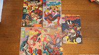 Five Web of Spiderman comic books arranged on a wooden table showing various colorful covers featuring Spiderman, Venom, and other characters.