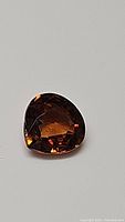 Top-down view of pear-shaped fire orange zircon gemstone on plain background showing color and clarity