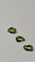 Three pear-shaped apple green Peridot gemstones arranged in a row showing facets and color.