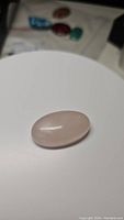 Photo of the oval cabochon cut rose quartz gemstone on a white background showing its soft pink color and smooth polished surface with some natural inclusions.