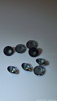 Eight dark iridescent faceted round calibrated mystic topaz gemstones on white background, showing size and shine.