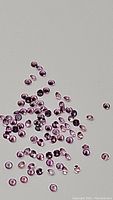 Heap of tiny pink sapphire gemstones scattered on grey surface, showcasing size and color
