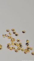Close-up photo showing multiple small yellow sapphire gemstones, round and oval shapes, diamond cut, reflecting light with good clarity