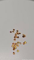 Photo showing numerous tiny round orange sapphires with diamond cut scattered on a white background.