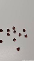 Thirteen small bullet-shaped cabochon garnet gemstones scattered on a white background, showing dark orange-red tones.