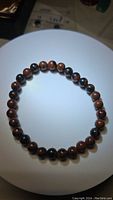 Close-up photo of the natural mahogany jasper bead bracelet placed on a white surface, showing the round polished beads in reddish-brown and black tones with natural jasper patterns.