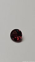 Close-up images of a single round cut Mozambique garnet gemstone showing deep cherry red color and facets.