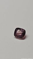Close-up image of 1 carat cushion cut pink-purple Myanmar spinel gemstone on a neutral background.
