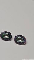 Pair of oval cut mystic topaz gemstones placed on a white background showing multi-color rainbow surface sheen.