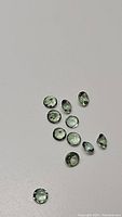 Multiple small round brilliant faceted green apatite gemstones on a white background.
