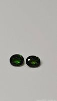 Pair of natural chrome diopside gemstones showing their oval cut and green color on white background.