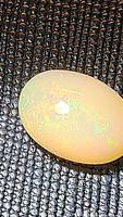 Close-up image of an oval natural Ethiopian opal on a textured black background showing rainbow play of color.