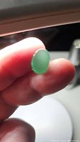 Close-up photo of a natural green aventurine oval cabochon gemstone held between fingers under light, showing the translucent green color and smooth polish.
