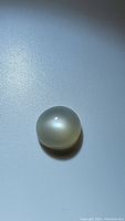 Close-up image of the round white moonstone cabochon showing its polished dome shape and milky translucent appearance with blue flash under lighting.