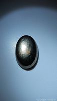 Oval-shaped pyrite cabochon gemstone with metallic golden surface under direct light showing reflection and texture.