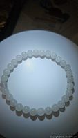 Photo of a natural white jade bead bracelet in a circular form on a white background, showing polished, uniform round beads with slight translucency.