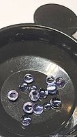Multiple small round cabochon purple iolite gemstones arranged in a container, showing their translucent purple colors and smooth surfaces.
