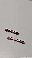 Photo of ten round cabochon raspberry pink sapphires with strong deep red tones on light background