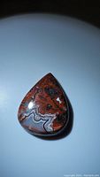 Top view of pear-shaped red crazy lace agate cabochon with distinct multicolored patterns and glossy finish.