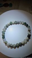 Photo of a natural tree agate bead bracelet on stretchy cord laid flat on a white surface showing green and white patterned beads.