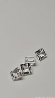 Four square cut white topaz gemstones showing clarity and cut details on plain background.