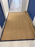 Full view of the rug placed on a white tiled floor, partially rolled on one end showing the underside.