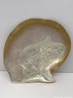 Front view of the carved mother of pearl shell showing the bird design and overall shell shape
