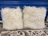Front view of two white Mongolian lamb fur pillows placed upright on a rug.