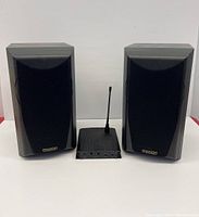 Pair of black vintage Mission bookshelf speakers flanking a black AV receiver with antenna on a white surface.