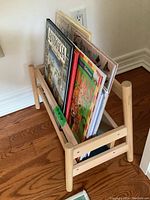 Front view of wooden book rack with books inside (books not included). Shows natural wood finish, slatted sides and bottom, and overall structure.