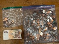 Three ziplock bags containing mixed coins and one 200 Czech koruna banknote laid out on wooden surface.