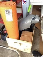 Photo showing the rolled orange exercise mat, gray textured exercise ball, cork yoga blocks, and part of the black kettlebell inside the wood crate.