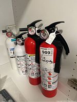 Four fire extinguishers arranged in a line showing color variation and pull pin detail.