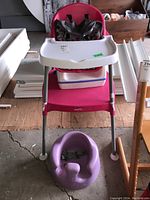 Red Evenflo baby high chair with white tray, black harness, and purple molded infant seat on floor in front