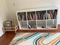 White IKEA Kallax bookcase shown against wall, filled with books and a few small items for size reference.