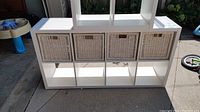 Front view of white Ikea Kallax bookcase with four wicker baskets inserted into the lower compartments
