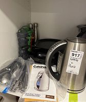 Photo showing Cuisinart kettle, cast iron fry pan, cutlery in plastic bag, and water bottles on shelf