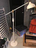 Full view of the white Ikea RANARP floor lamp standing on the floor near household items.