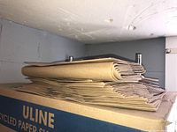 Stacked recycled paper shopping bags on top of a large Uline branded cardboard box.