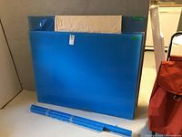 Seven plexiglass sheets stacked together, wrapped in blue protective film; one larger sheet at the back and six smaller sheets in front.