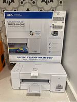 Photo showing the original box of the Brother MFC-J1205W color inkjet printer with the printer displayed in front.