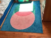 Full view of the blue acrylic area rug with large overlapping circular patterns in pink, red, and green under natural lighting.